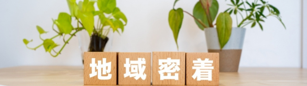 木製ブロックに白文字で『地域密着』と記載され、背後には観葉植物が並ぶナチュラルなイメージ