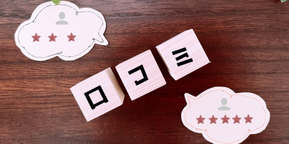 木製ブロックに「口コミ」と書かれ、左右に星の評価が描かれた吹き出しが配置されている。