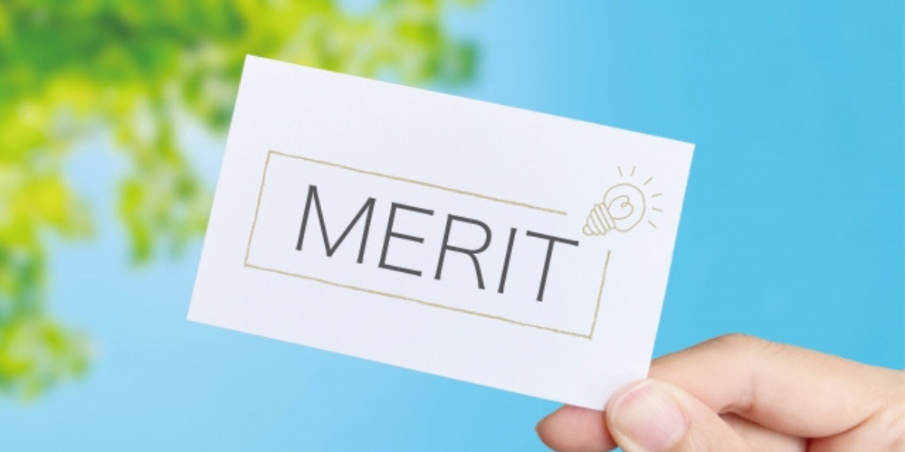 青空と木の葉を背景に「MERIT」と書かれたカードを持つ手元の画像
