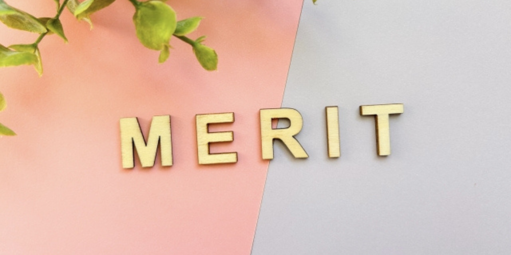 ピンクとグレーの背景の上に、木製の文字で「MERIT」と並べられている。