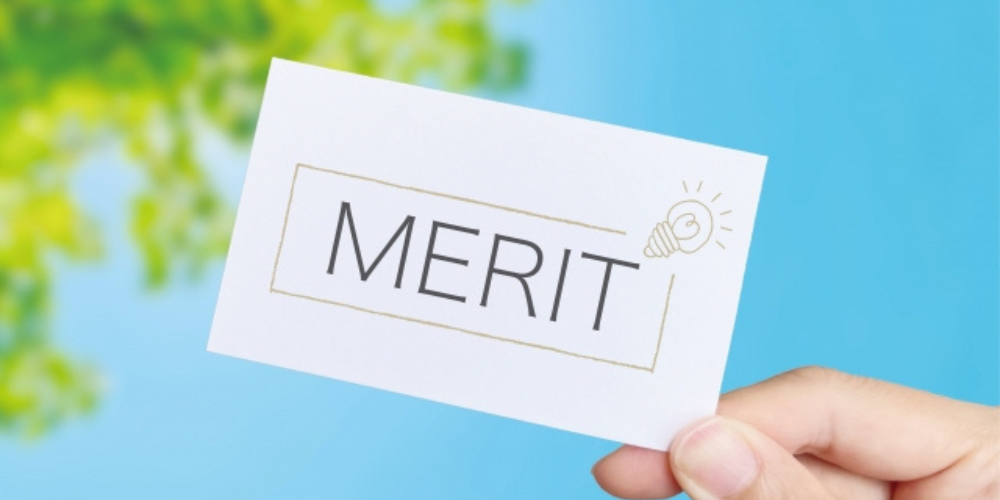 青空と緑を背景に「MERIT」と書かれたカードを指で持っている様子