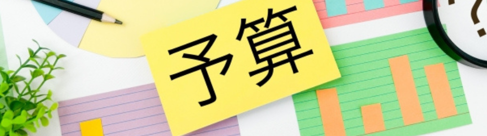 「グラフや円チャートの上に黄色い付箋で『予算』と書かれている、緑の観葉植物も配置」