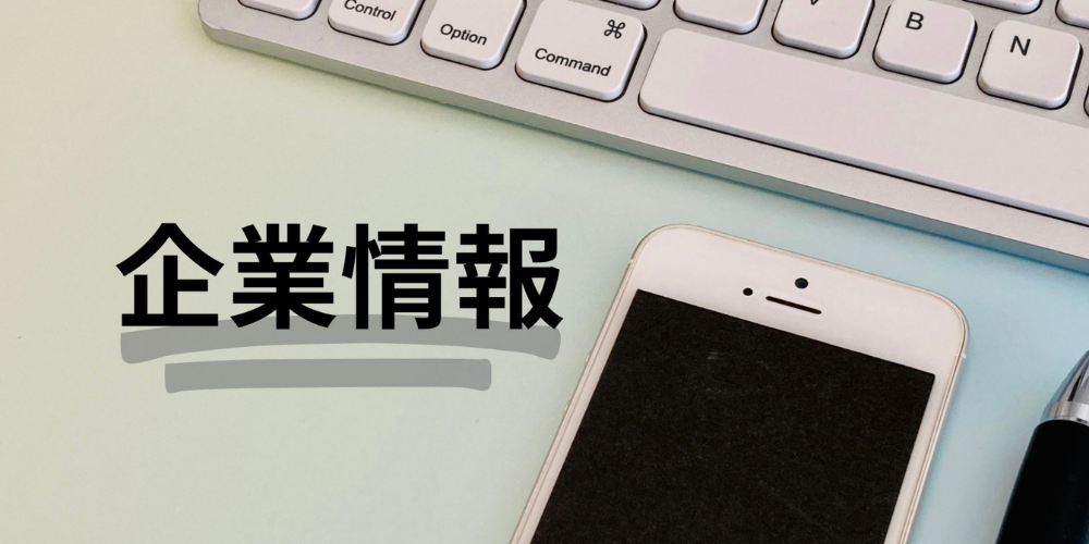 企業情報の文字と共に、パソコンのキーボード・スマートフォン・ボールペンが並べられたビジネスイメージの写真