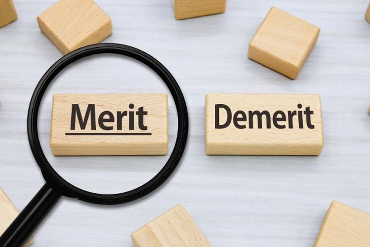 木製ブロックに書かれた『Merit』と『Demerit』の文字、虫眼鏡でメリット側が強調されたイメージ