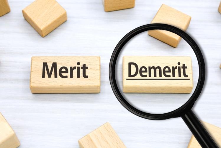 木製ブロックに書かれた『Merit』と『Demerit』、虫眼鏡でデメリット側が強調されている比較イメージ