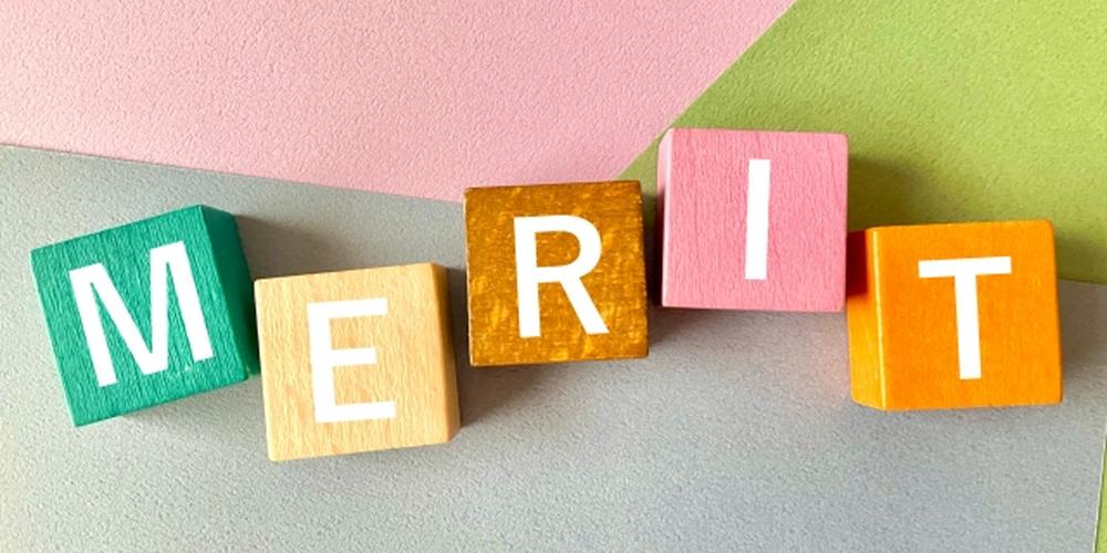 カラフルな積み木で「MERIT」と並べられた文字、背景にはパステルカラーの紙が敷かれている