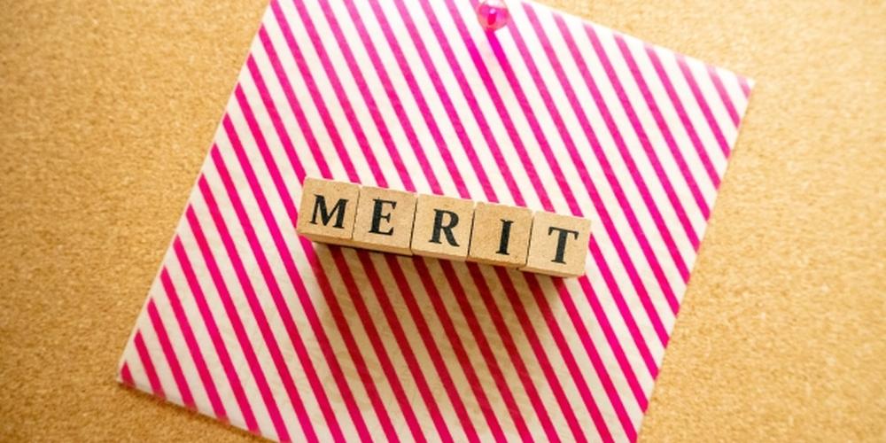 ピンクのストライプ模様の紙の上に並べられた「MERIT」の文字ブロック、コルクボードに留められているイメージ