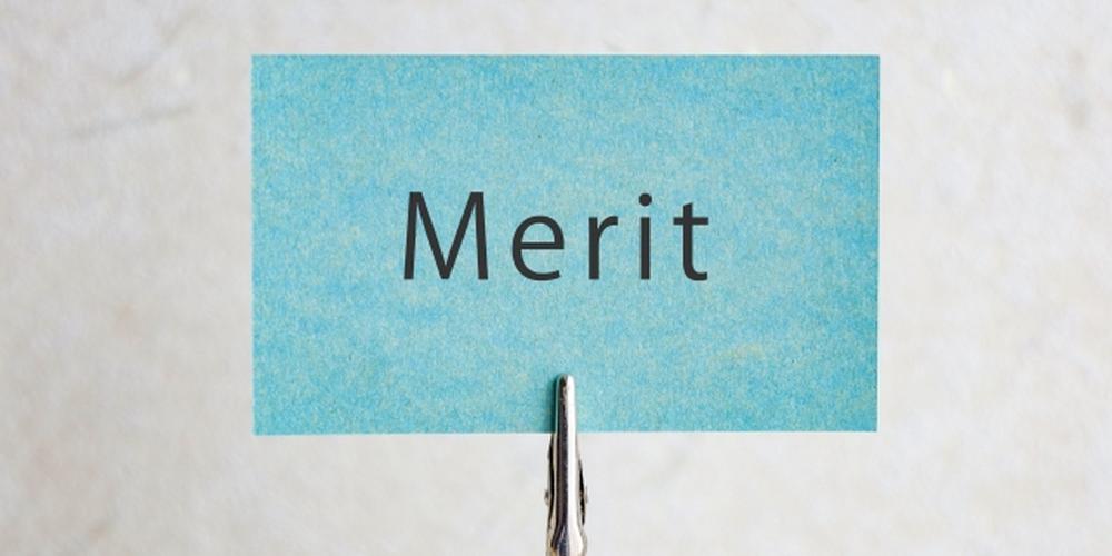 青い紙に「Merit」と書かれ、金属クリップで立てられているシンプルな背景のイメージ