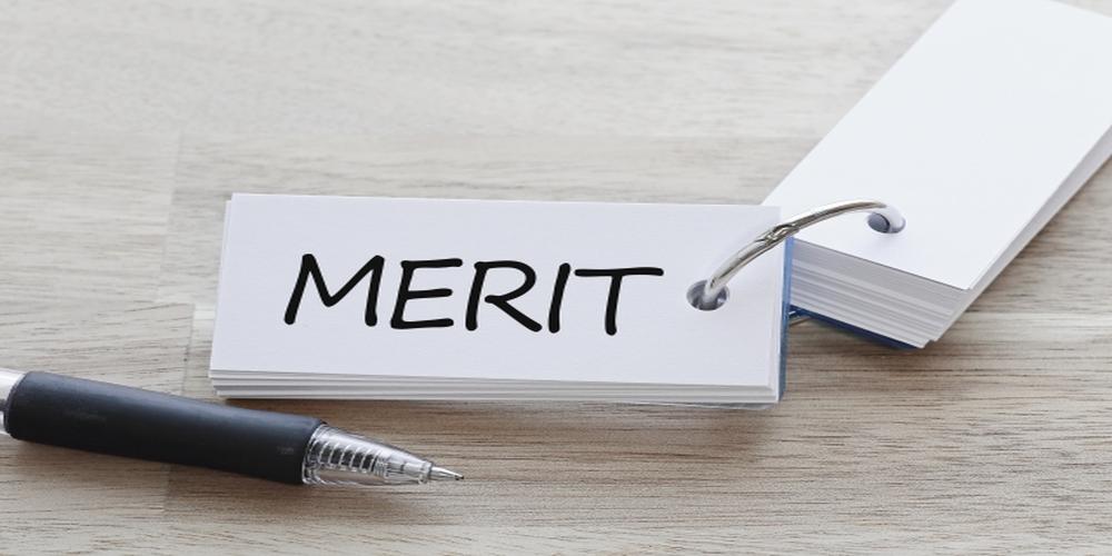 「MERIT」と書かれたカードリングと黒いボールペンが置かれた木目調のデスク。
 