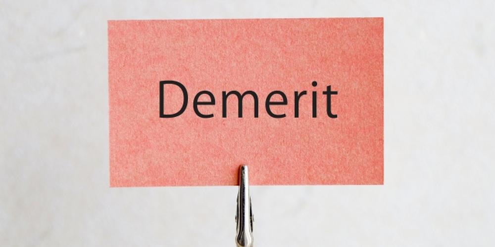 赤い紙に「Demerit」と書かれたカードが金属クリップで立てられている、シンプルな背景のイメージ