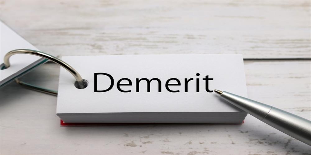 「Demerit」と書かれたカードリングと銀色のボールペンが置かれた白いデスク。
 