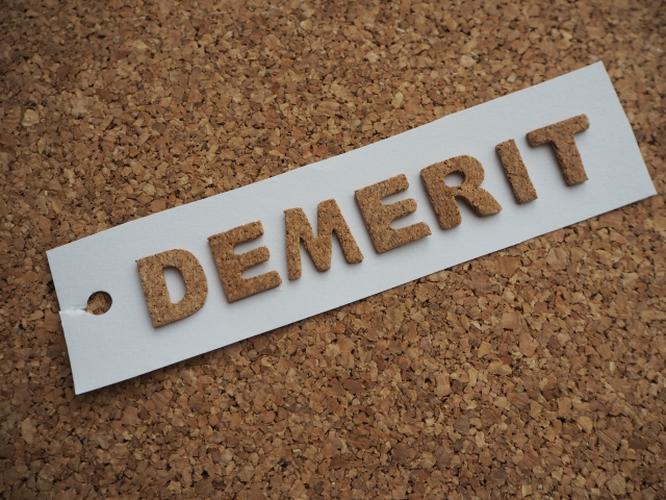「コルクボードの上に置かれた白いタグに『DEMERIT』とコルク素材の文字で書かれたシンプルなイメージ」