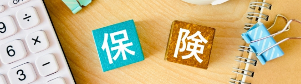 木製の机の上に「保険」と書かれたキューブと電卓、文房具が置かれている。