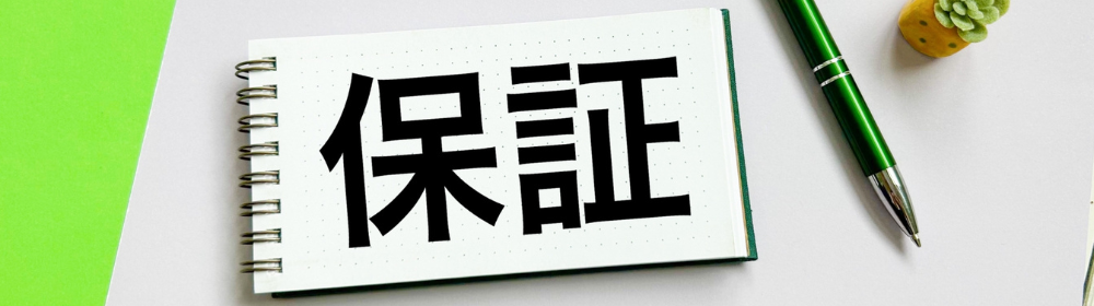 ノートに大きく「保証」と書かれ、横に緑色のペンが置かれたイメージ