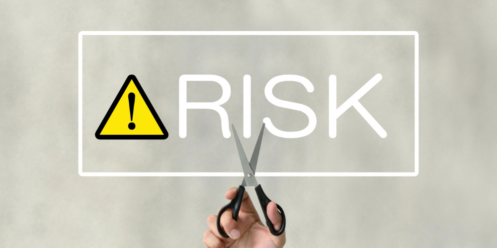 「RISK」という文字をハサミで切り、リスクを断ち切るイメージ