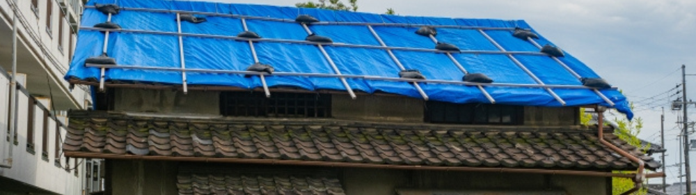 雨漏り対策でブルーシートをかぶせられた古い住宅の屋根の様子。