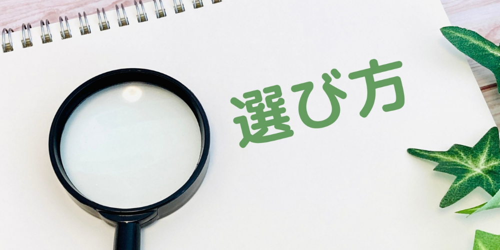 ノートの上に虫眼鏡と「選び方」という文字、観葉植物が置かれている