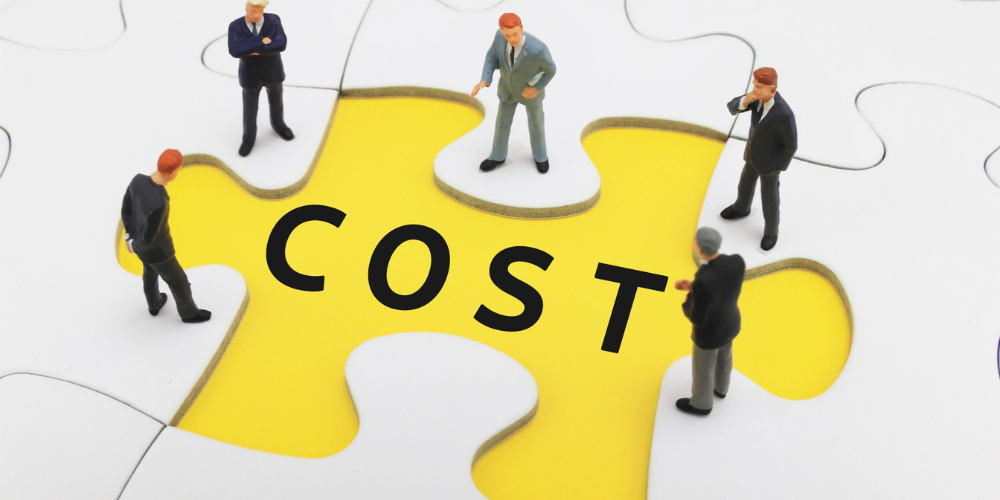 「COST」と書かれた大きなジグソーパズルの上で、ミニチュアのビジネスマンたちが議論している