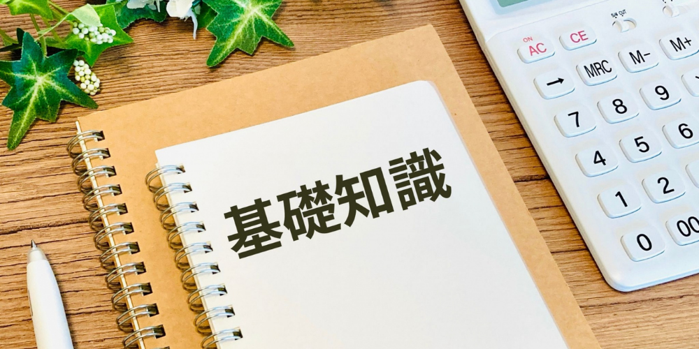 木目デスクに置かれたスパイラルノートに「基礎知識」と書かれ、横に電卓とペン、アイビーの葉
