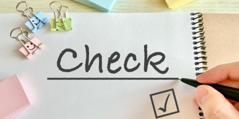 ノートに「Check」と書かれた手書き文字、チェックマークの入ったボックスとカラフルな文房具