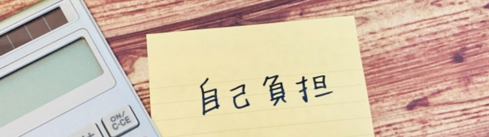 木目のテーブルに置かれた電卓と「自己負担」と書かれたメモの画像