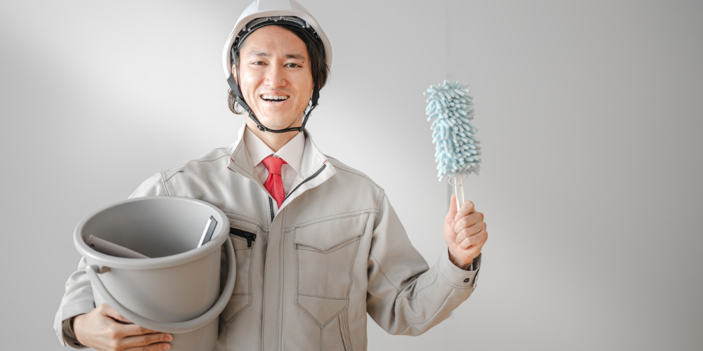 ヘルメット作業服の男性がバケツとハンディモップを掲げて微笑むポートレート