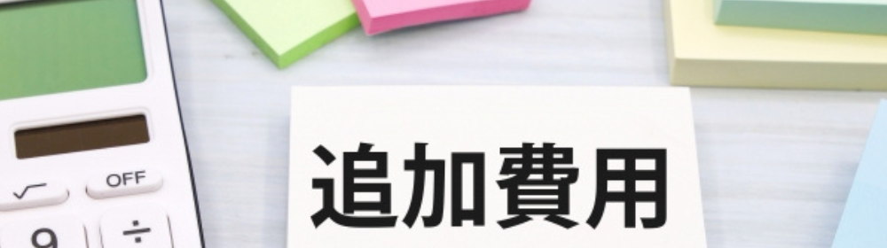 電卓と付箋の横に置かれた「追加費用」と書かれたカード。予算や見積もりに関する文脈。