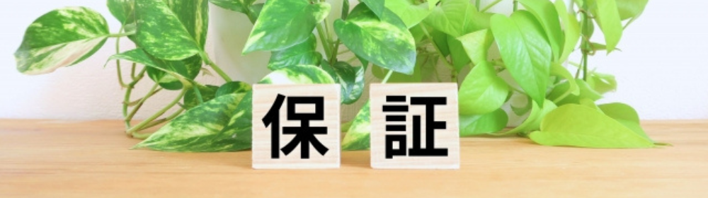 観葉植物の前に置かれた「保証」の文字が書かれた木製ブロック。安心感を表現。