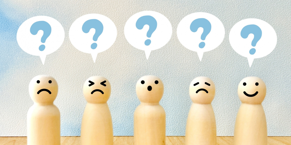 さまざまな表情の木製人形の上に、クエスチョンマークの吹き出しが並んでいる