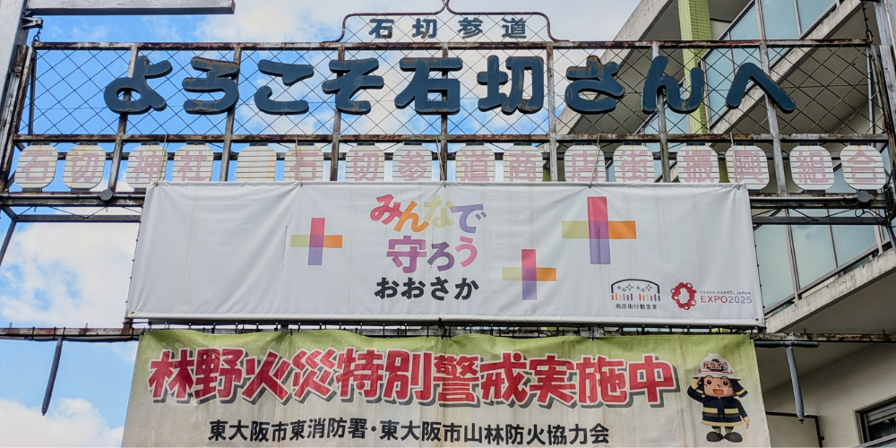 「ようこそ石切さんへ」と掲げたアーケード看板と、EXPO 2025ロゴ入り防災・防火啓発バナー