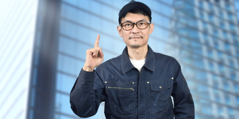作業服とキャップ姿で人差し指を立てる塗装職人のポートレート