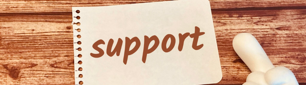 木目の机に置かれた「support」のメモと親指アップのポインター