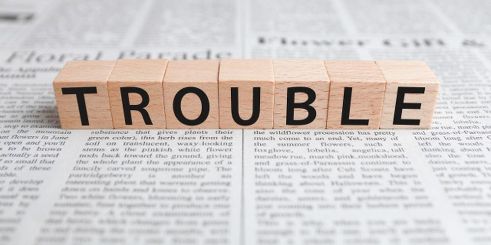 新聞の上に並べられた「TROUBLE」の文字ブロックのイメージ写真