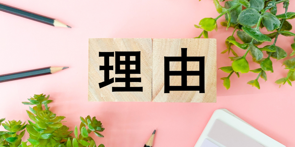 ピンクの背景に置かれた「理由」と書かれた木製ブロック