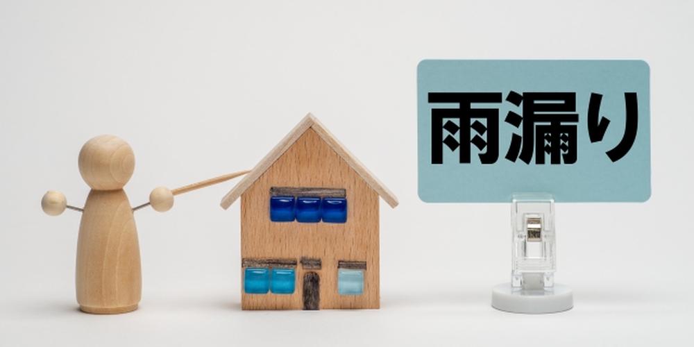 雨漏りを示すサインと小さな家の模型、木製人形が家を指差している様子