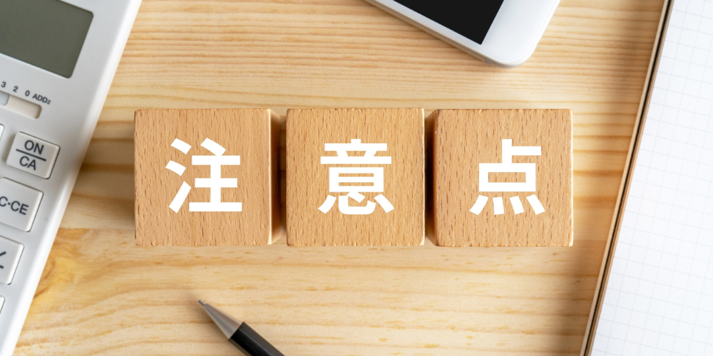 木目のデスクで電卓とノートの間に並んだ木製ブロックに「注」「意」「点」と白字で書かれた注意喚起イメージ