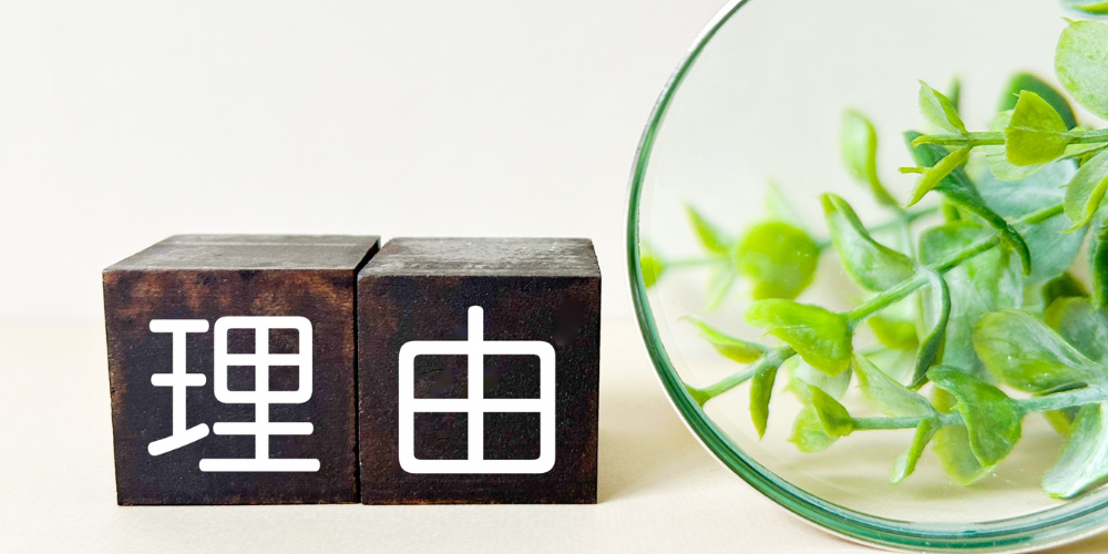 ダークブラウンの木製ブロック2つに白字で「理」「由」と並べ、右側にグリーンの植物と拡大鏡が置かれた「理由」強調イメージ
