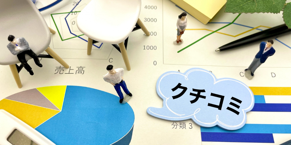 チャート資料の上に小さな人形フィギュアが立ち、「クチコミ」と書かれた吹き出しを添えたマーケティング分析イメージ