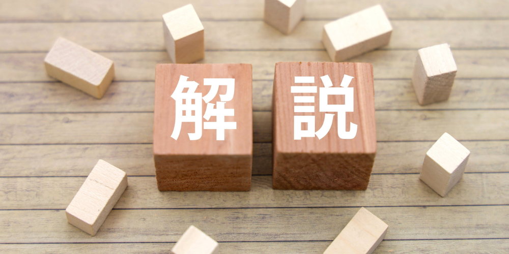 木製の小さな立方体ブロックに白抜きで「解説」と描かれ、背景に多数の小さな木製ブロックが散らばっている