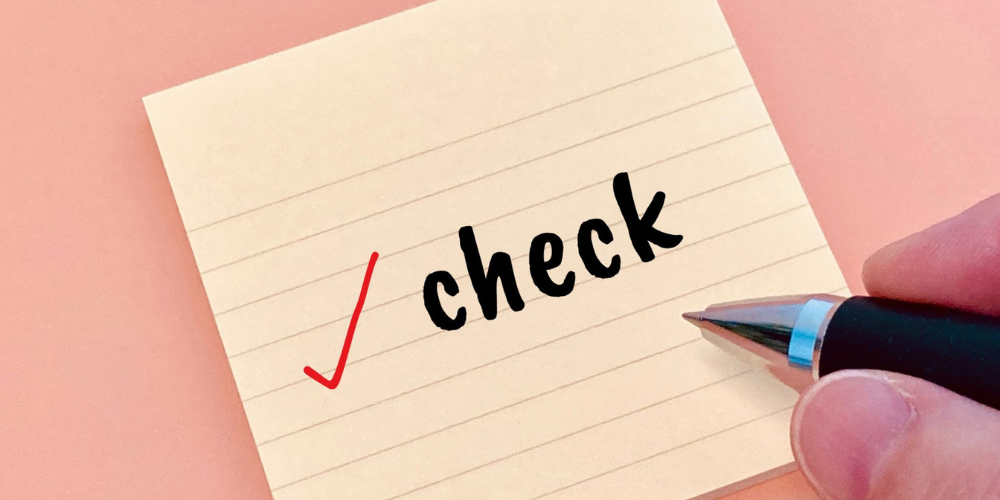 淡いピンクの背景に方眼メモ用紙が置かれ、その上に赤いチェックマークと「check」という黒い手書き風文字