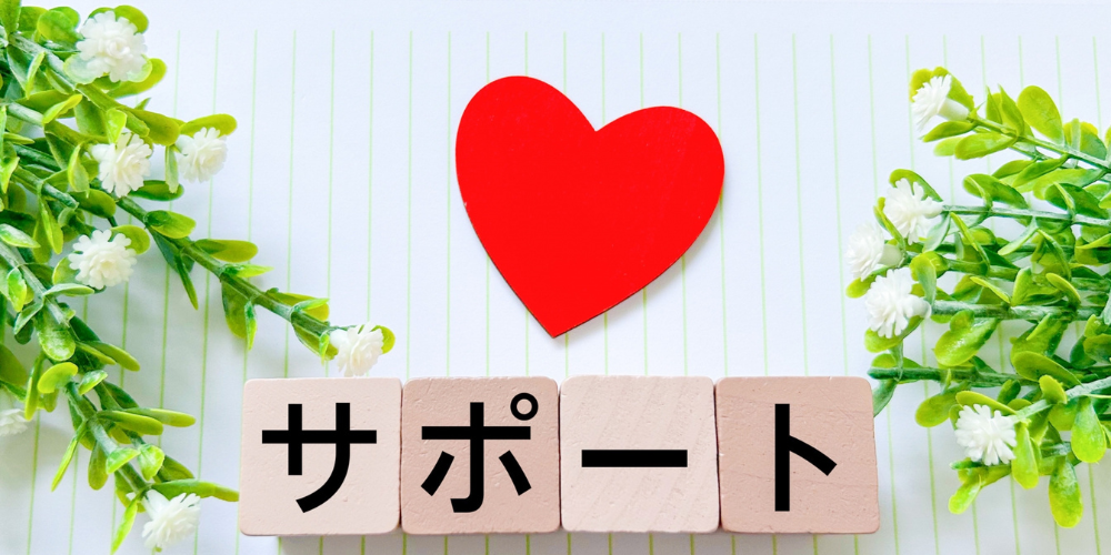 白い背景に緑の植物をあしらい、木製ブロックで「サ」「ポ」「ー」「ト」と並べ、上部に赤いハートを添えたサポート強調イメージ